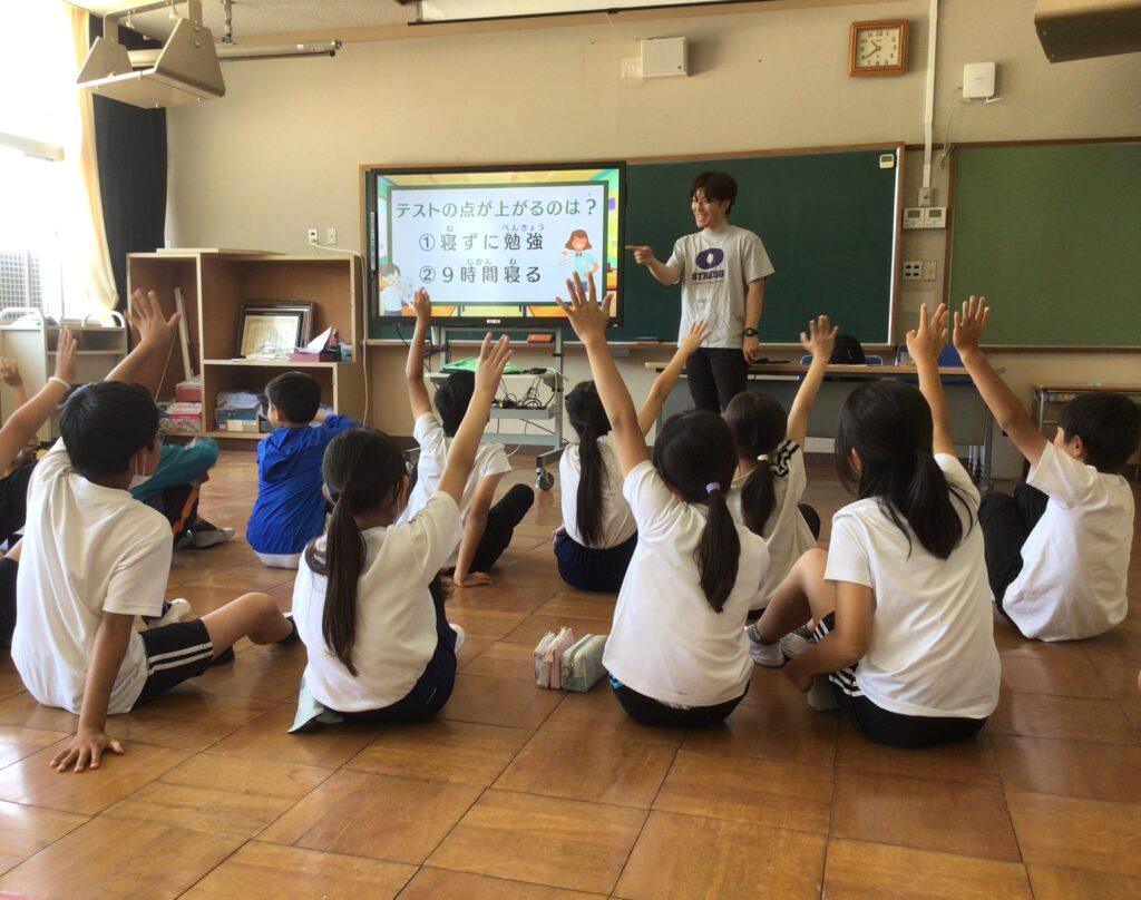 手を挙げて睡眠クイズに参加する小学生